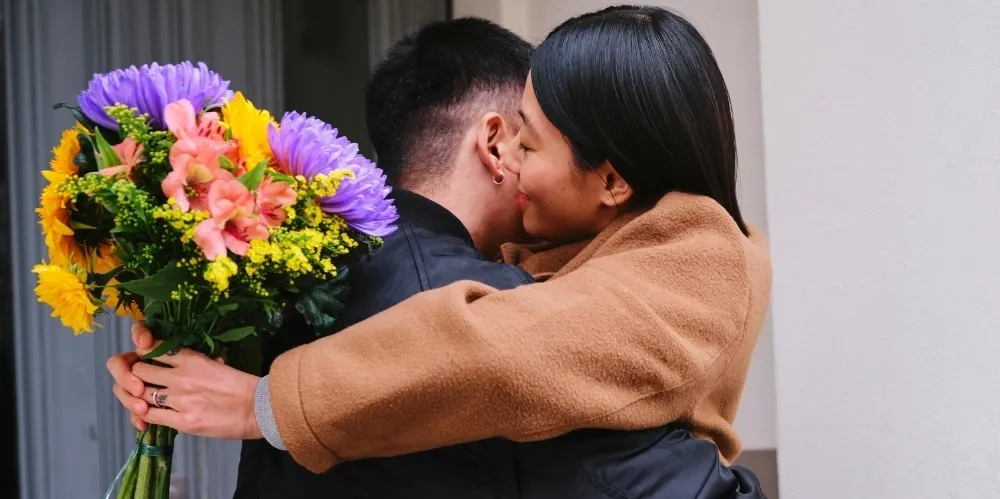 rs=w_1000,h_500,cg_true (1) A man and woman hugging each other holding flowers.